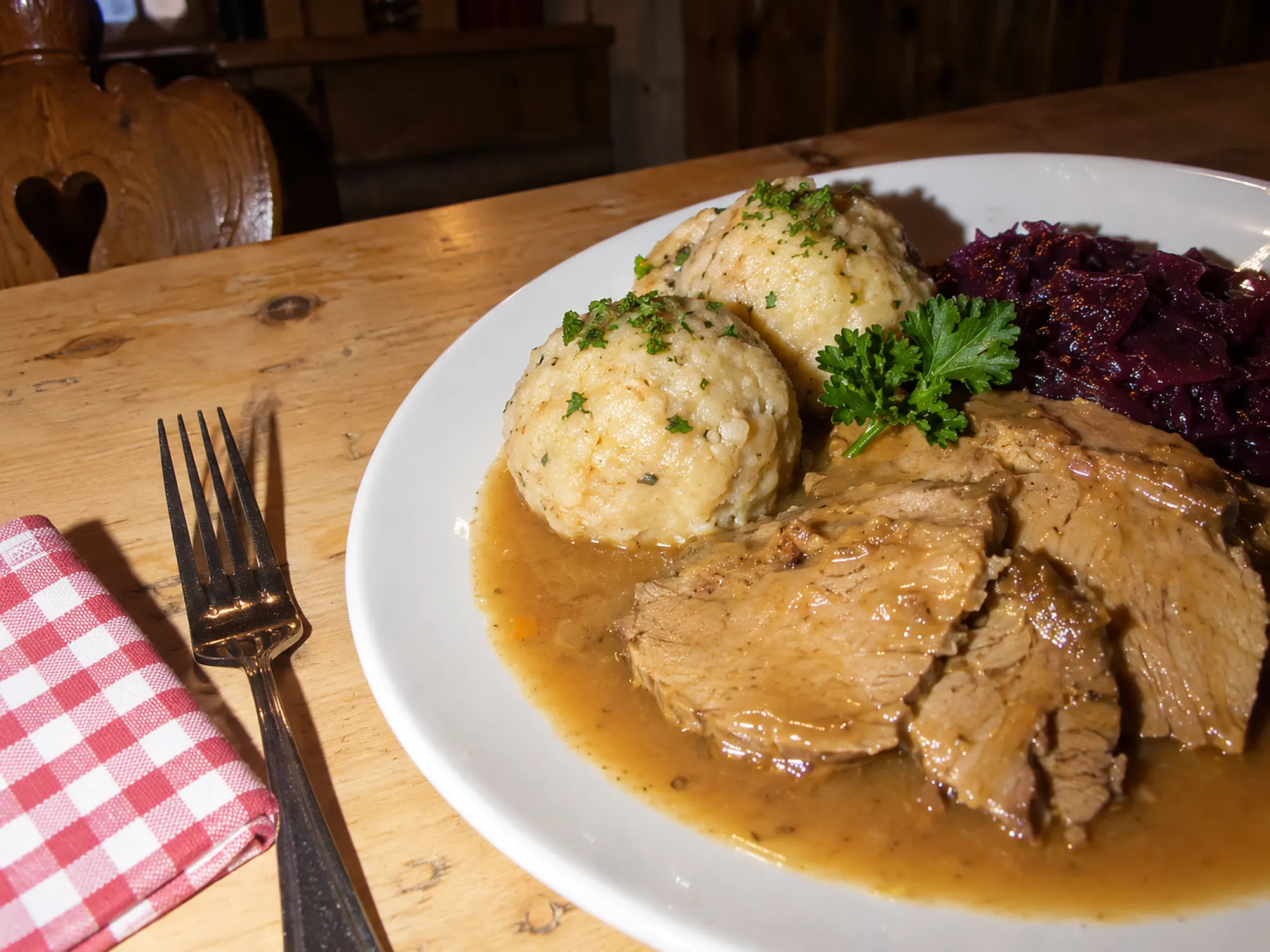 Teller mit Kalbsbraten in heller Soße, zwei Semmelknödeln und Blaukraut (KI-Illustration)