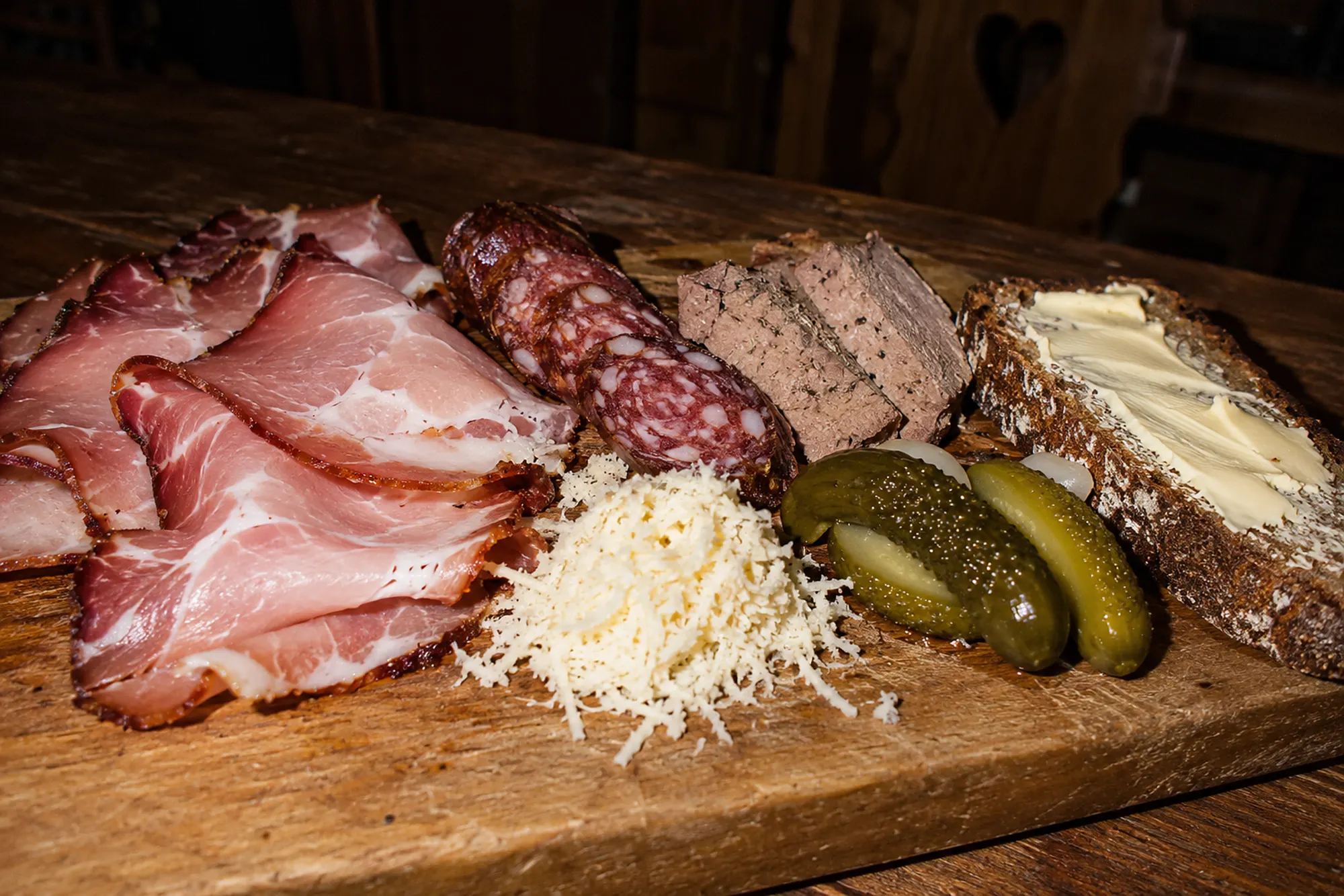 Brotzeitbrett mit Schinken, Wurst, Leberpastete, Kren, Essiggurken und Bauernbrot (KI-Illustration)